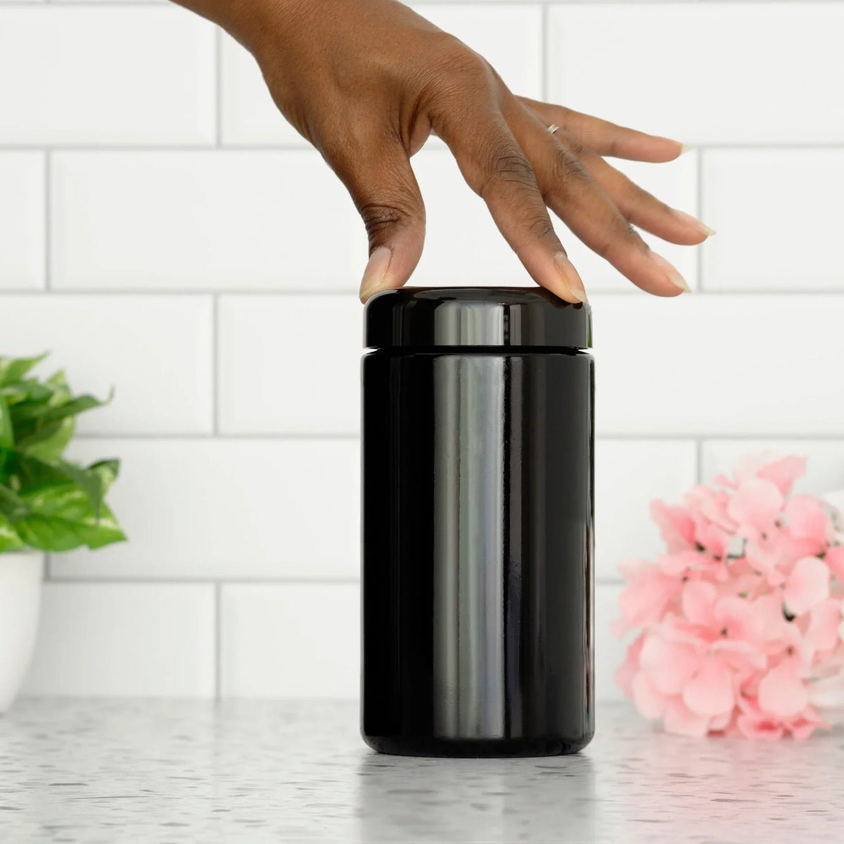 A hand extends toward a sleek black jar resting on a kitchen counter, ready to grab its contents