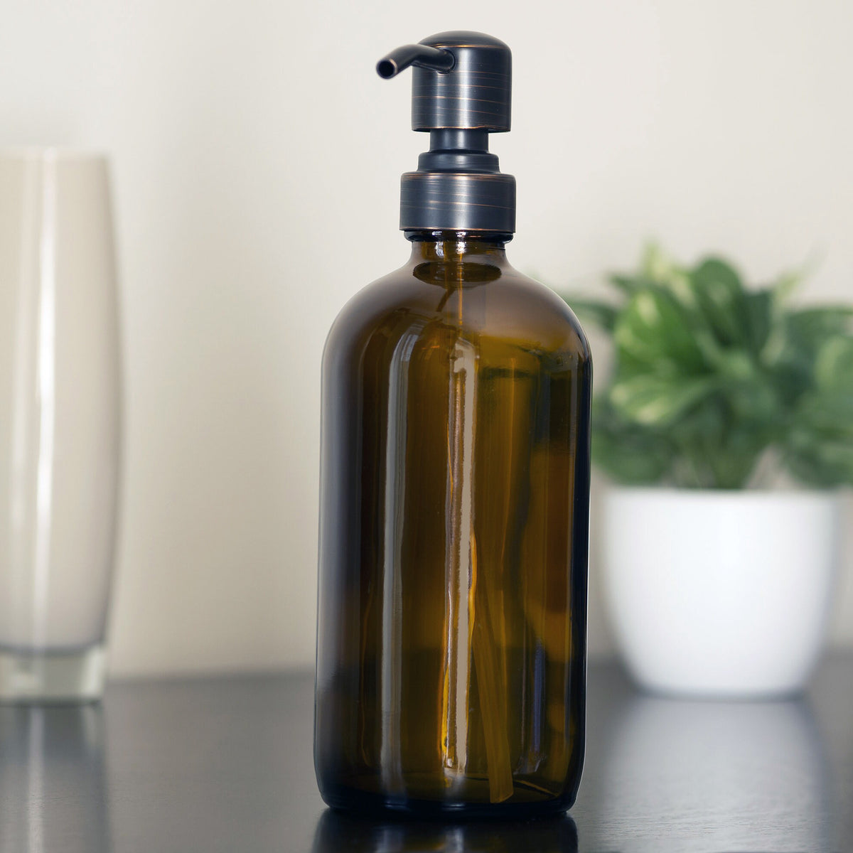 Amber bottle with pump on black table, tan wall, plant in white pot. 