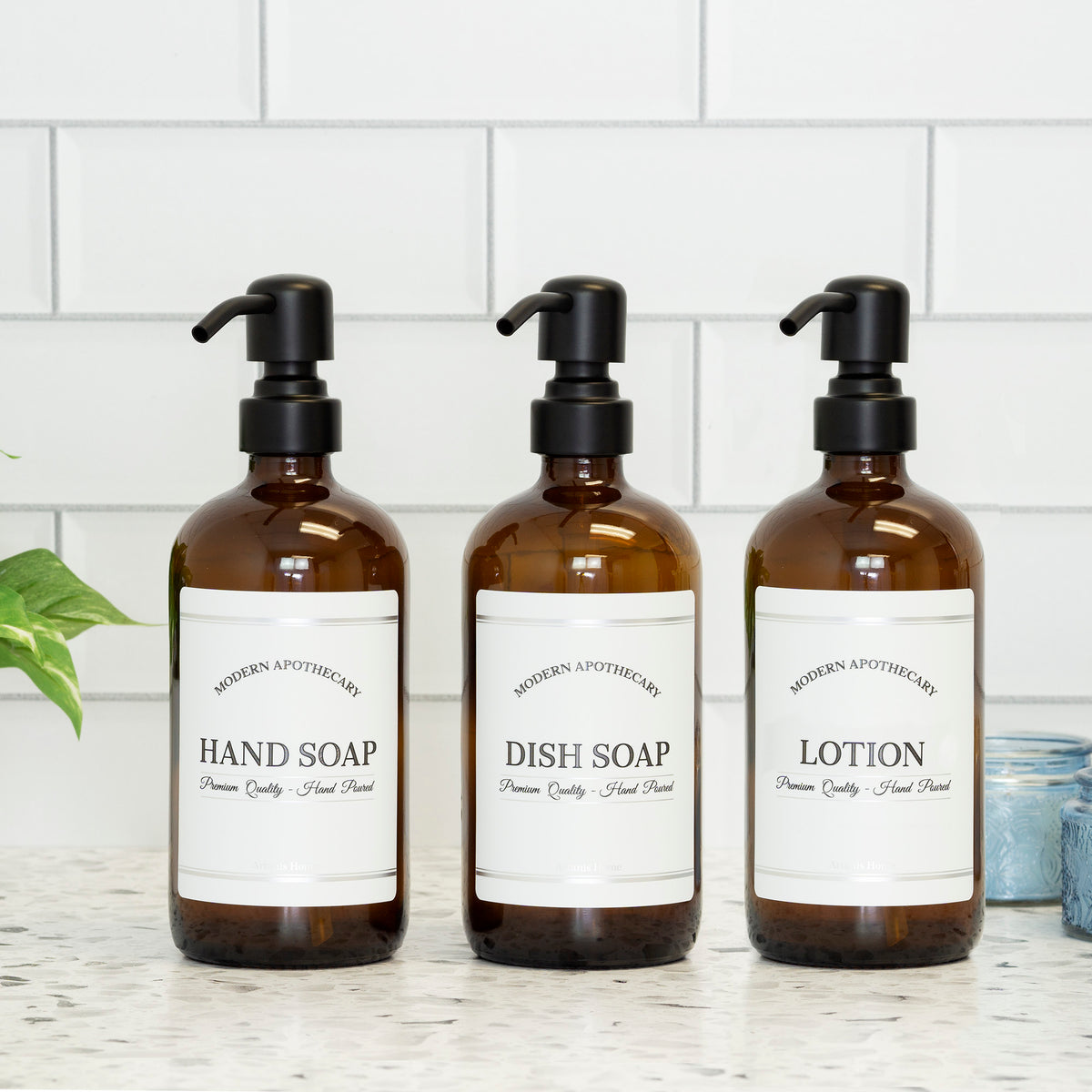 amber glass hand soap, dish soap, and lotion dispenser set with black stainless steel pumps and labels.